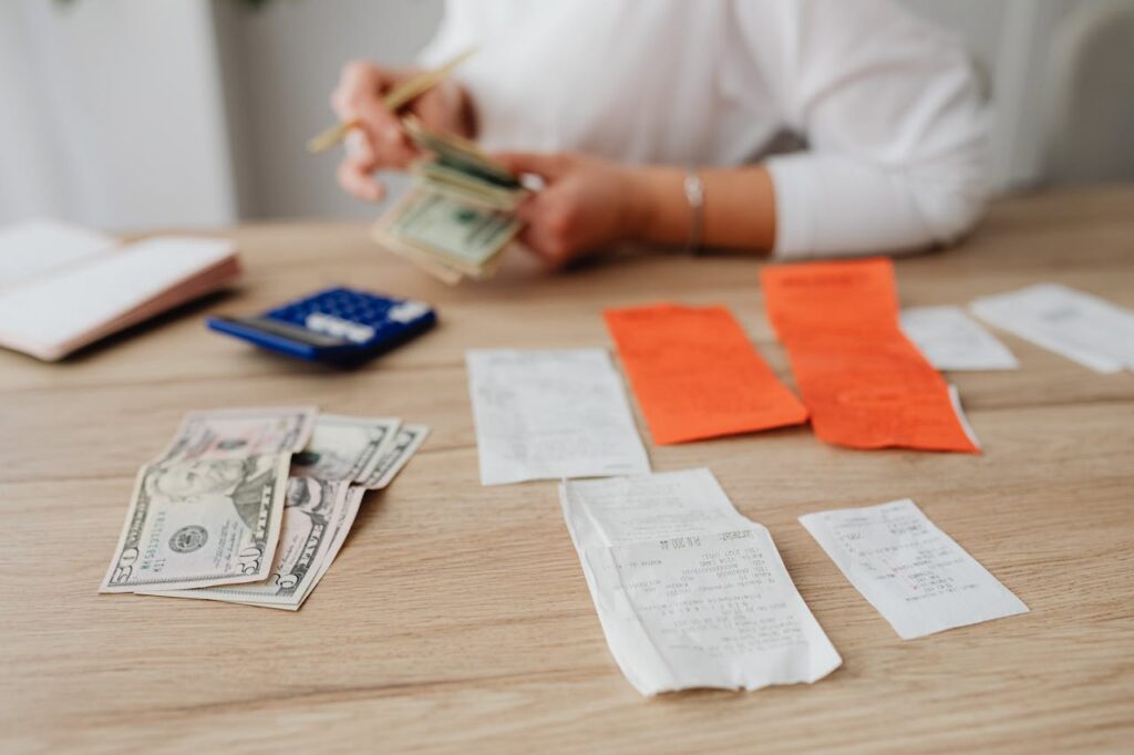 Photo of a woman counting paper money. shes at a table that has money, a calculator, and receipts.